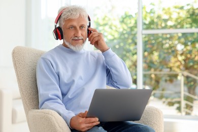 Senior man in headphones using laptop at home