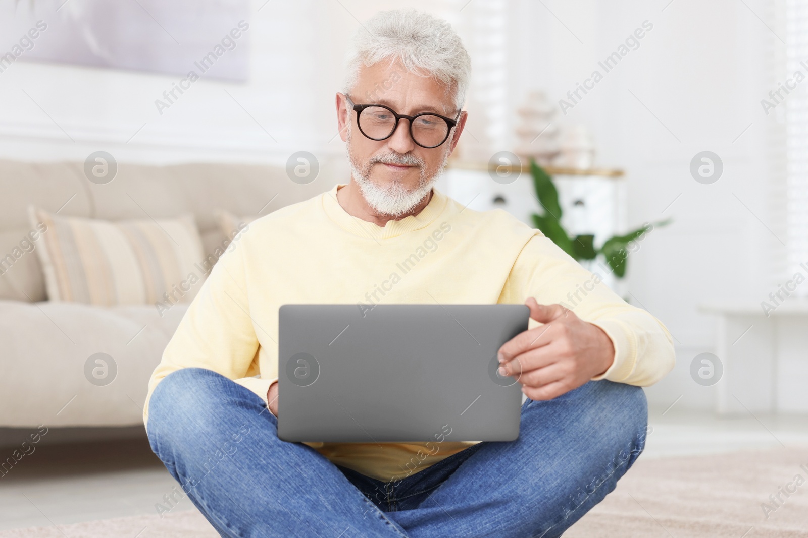 Photo of Senior man using laptop on floor at home