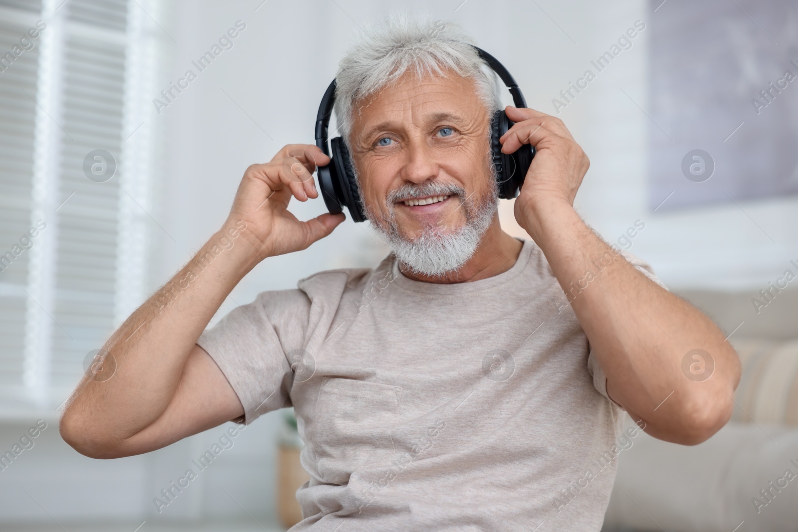 Photo of Smiling senior man in headphones listening to music at home