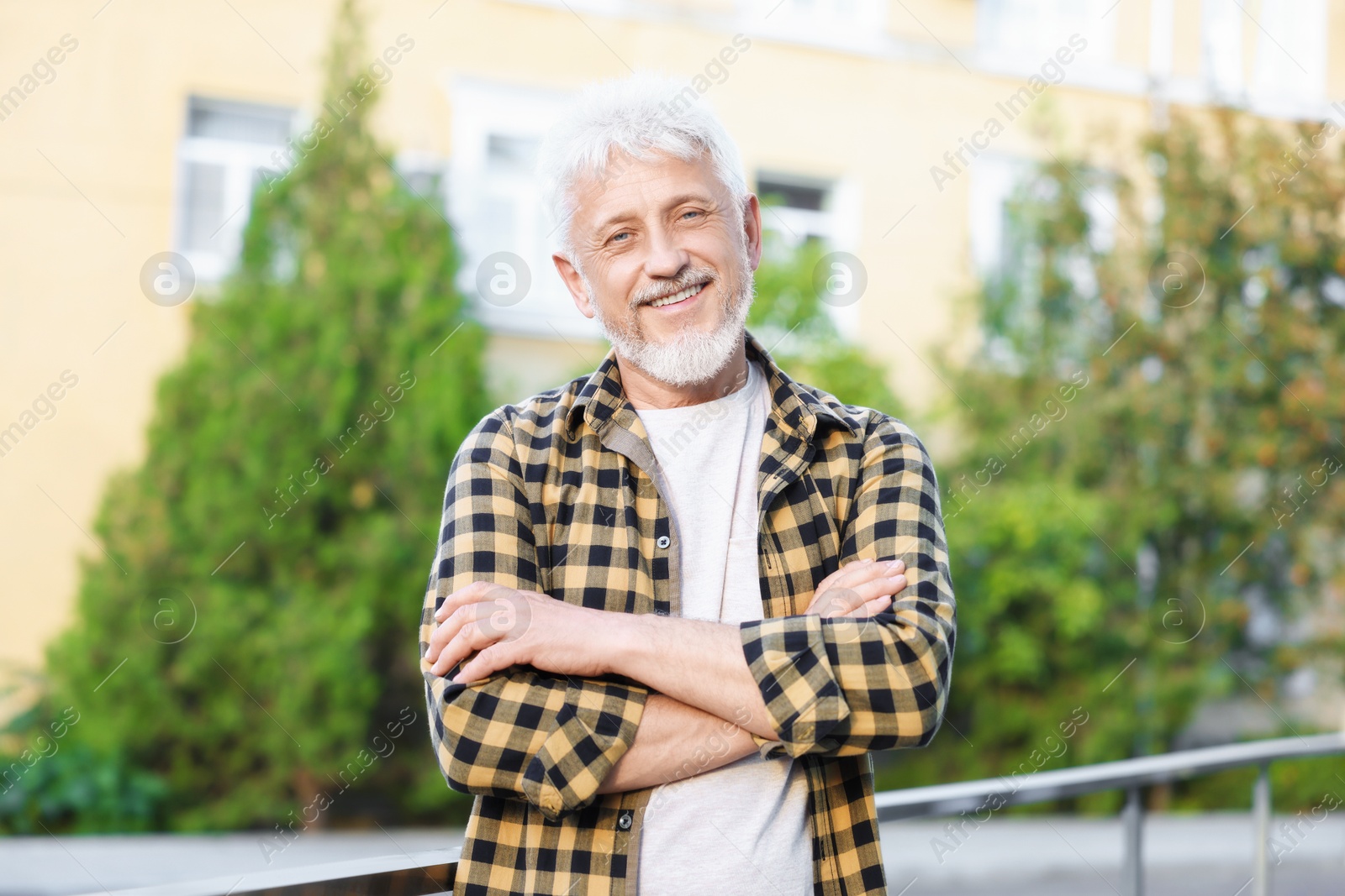 Photo of Portrait of smiling senior man with crossed arms outdoors