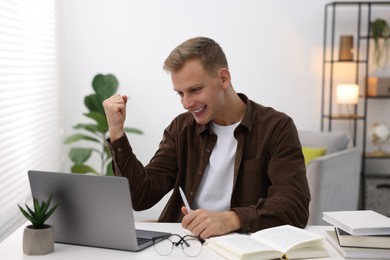 Photo of Preparing for exam. Cheerful student with laptop at table indoors