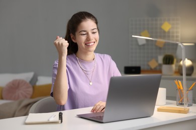 Photo of Preparing for exam. Cheerful student with laptop at table indoors