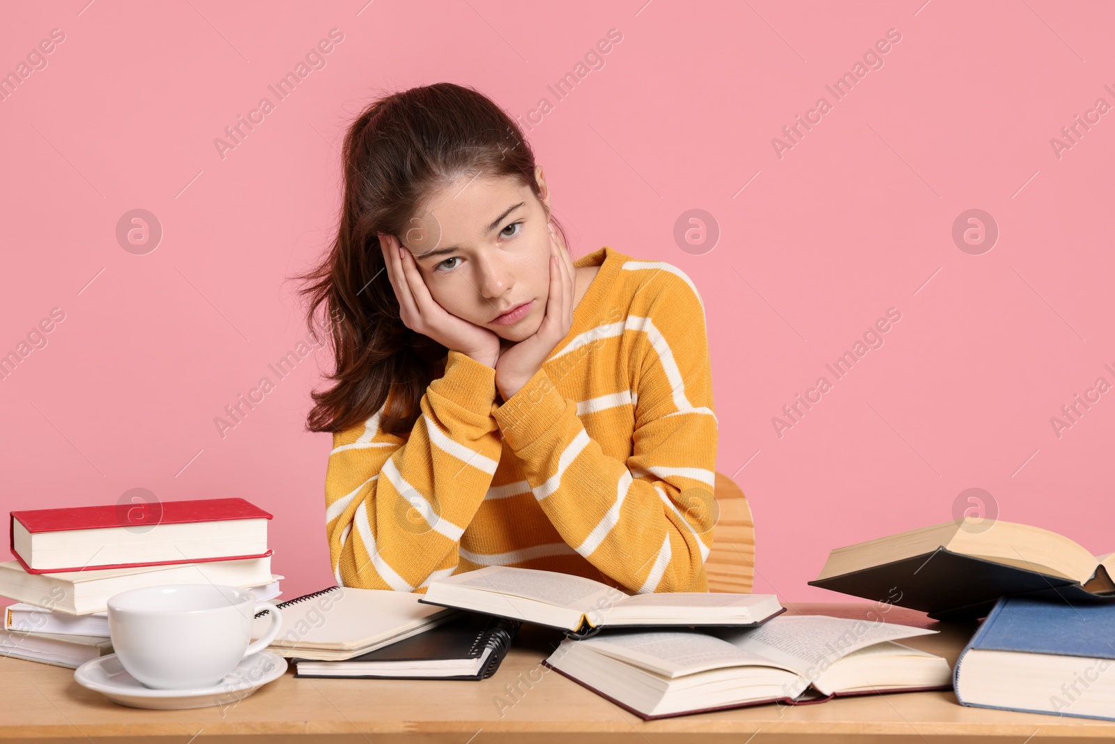 Photo of Preparing for exam. Student with books at table against pink background