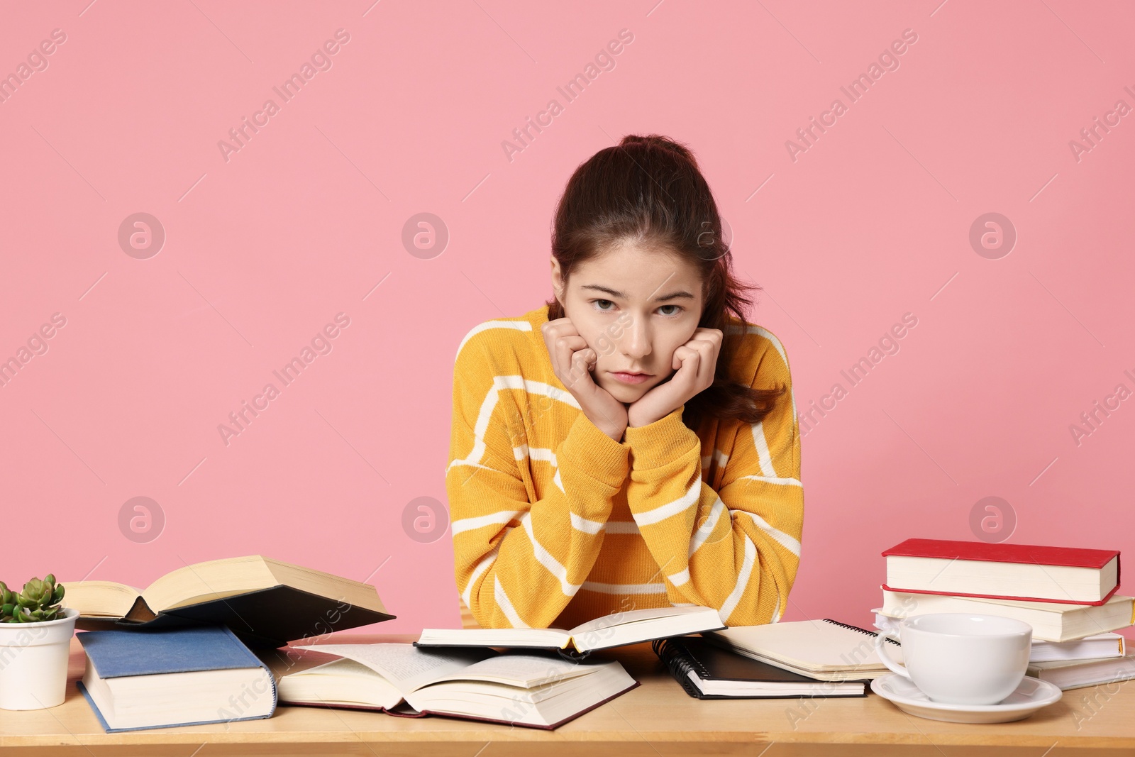 Photo of Preparing for exam. Student with books at table against pink background