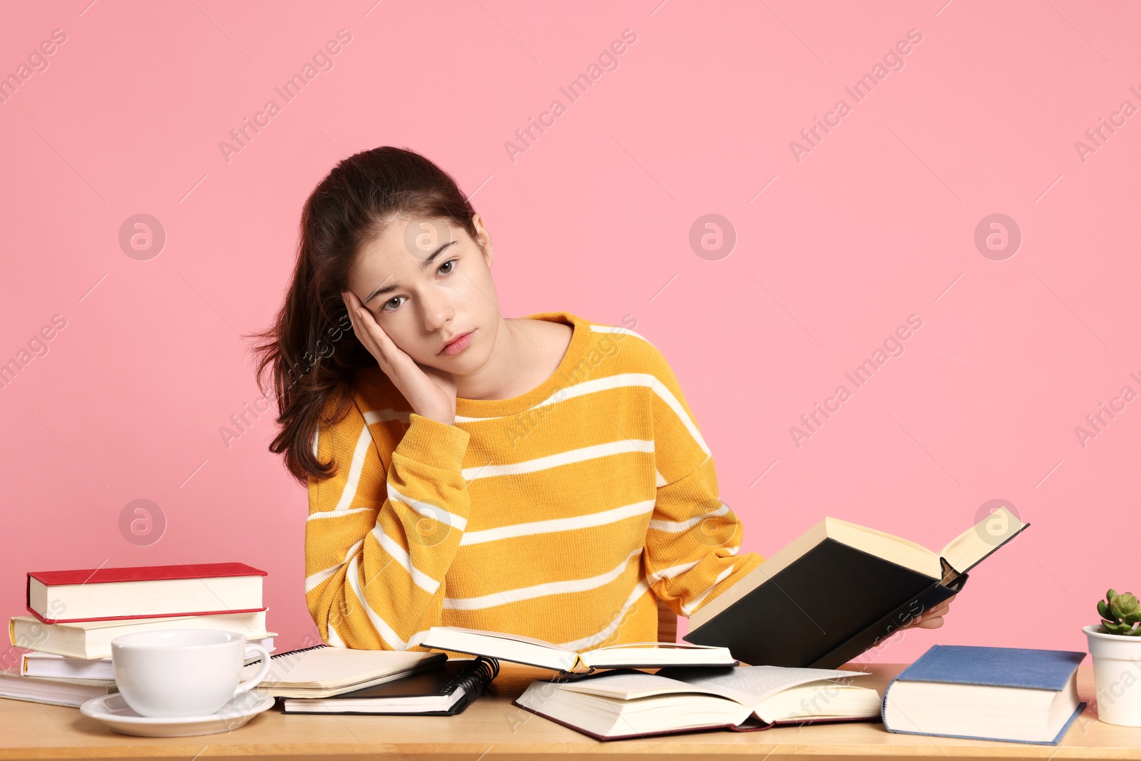 Photo of Preparing for exam. Student with books at table against pink background