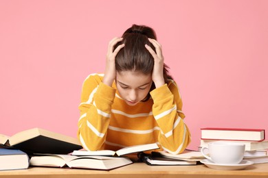 Photo of Preparing for exam. Student with books at table against pink background