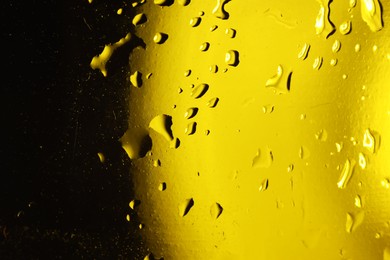 Photo of Water drops on dark yellow glass surface, macro view