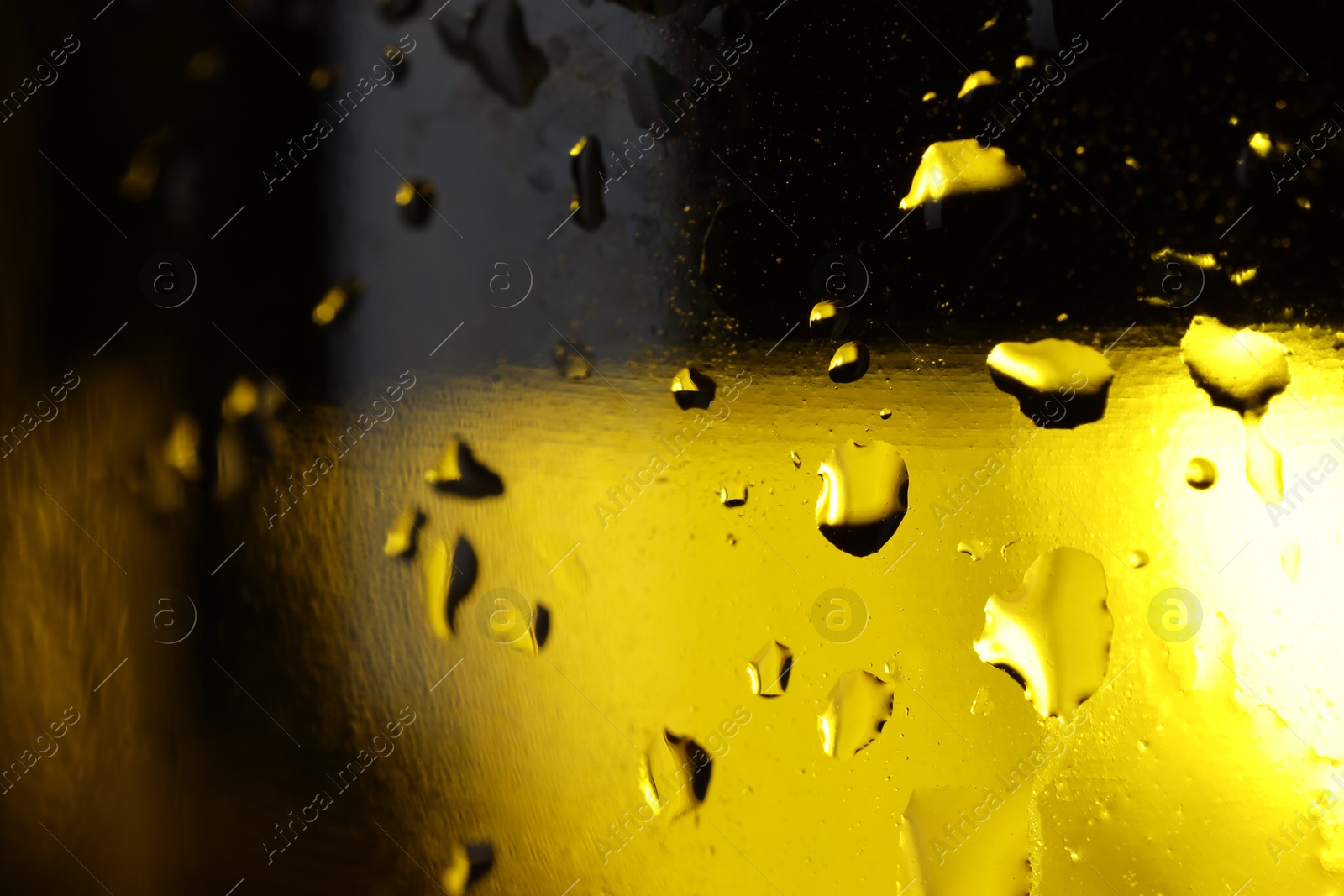 Photo of Water drops on dark yellow glass surface, macro view