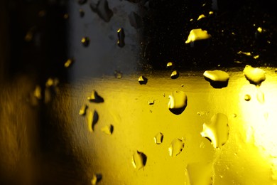 Photo of Water drops on dark yellow glass surface, macro view