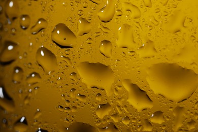 Photo of Water drops on dark yellow glass surface, macro view