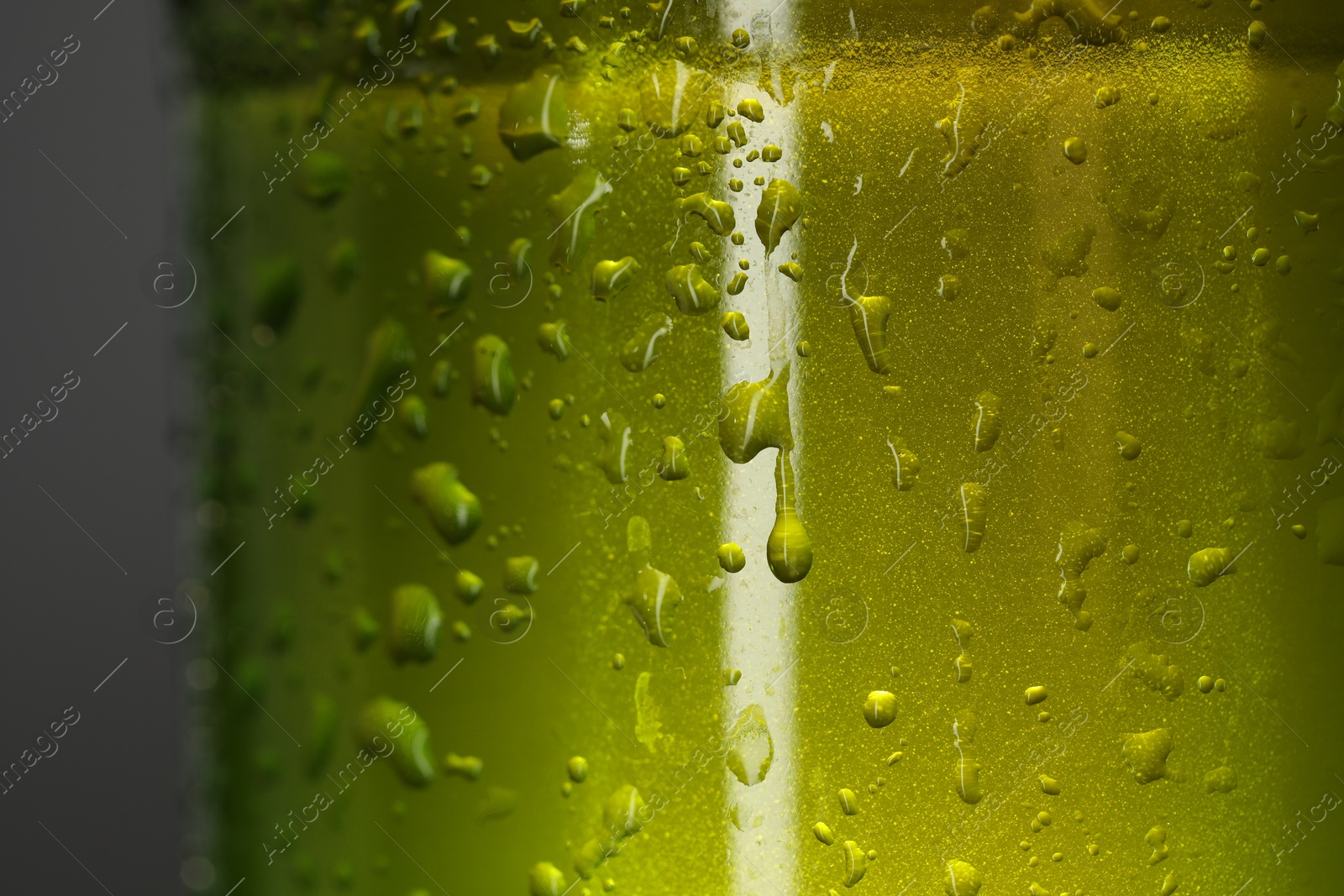 Photo of Glass bottle with condensation drops on grey background, macro view