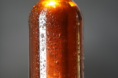 Photo of Glass bottle with condensation drops on grey background, closeup