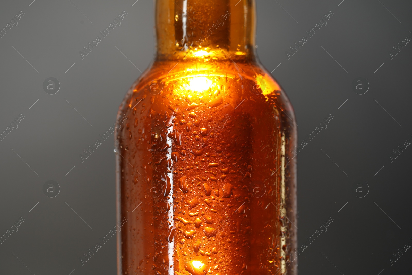 Photo of Glass bottle with condensation drops on grey background, closeup