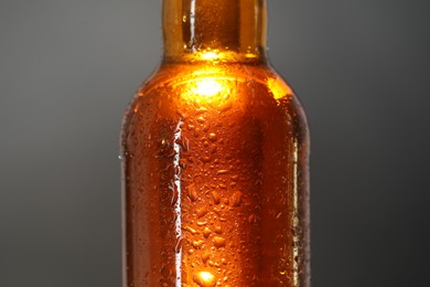 Photo of Glass bottle with condensation drops on grey background, closeup