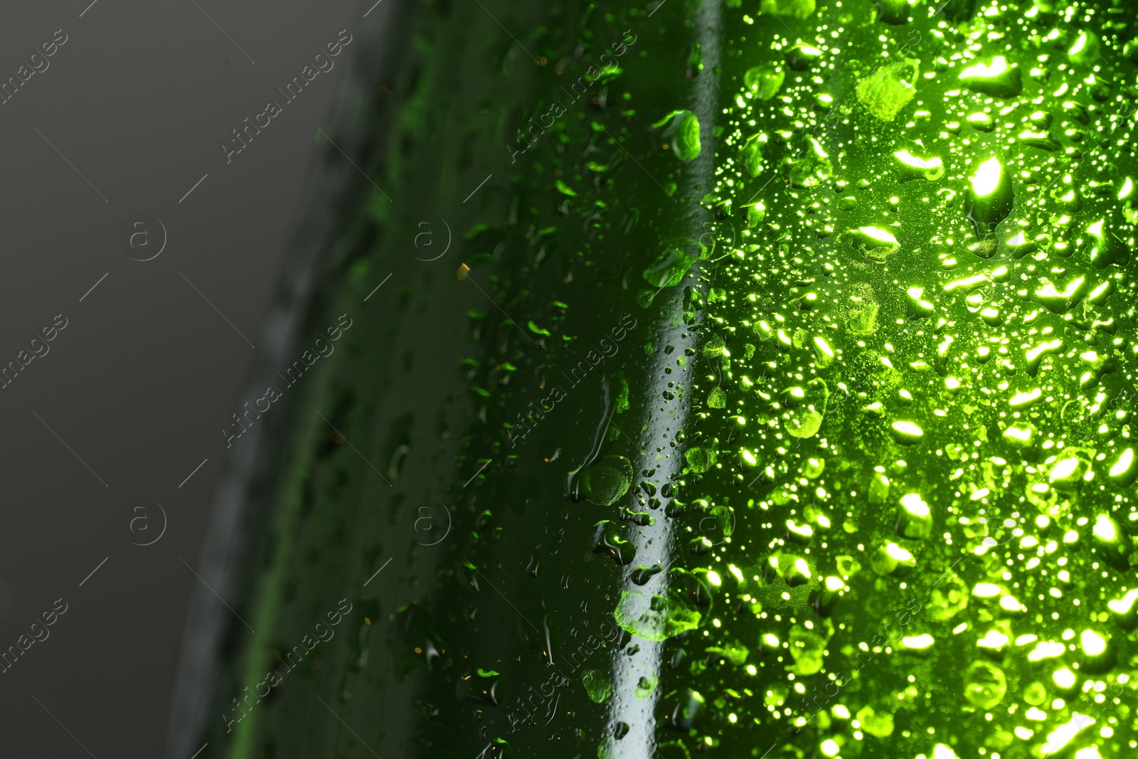 Photo of Glass bottle with condensation drops on grey background, macro view