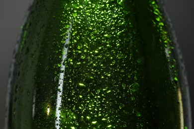 Photo of Glass bottle with condensation drops on grey background, macro view