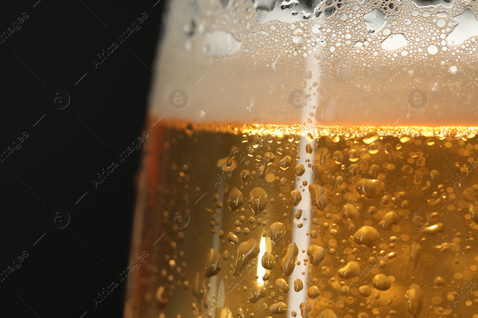 Photo of Glass of beer with condensation drops on black background, macro view