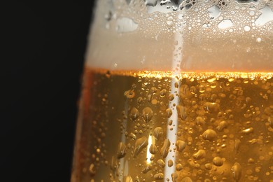 Photo of Glass of beer with condensation drops on black background, macro view