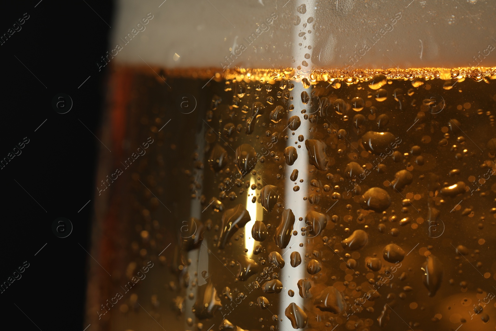 Photo of Glass of beer with condensation drops on black background, macro view