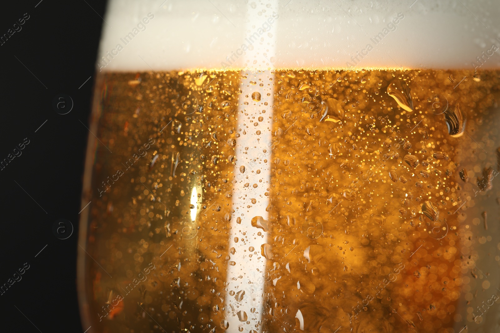 Photo of Glass of beer with condensation drops on black background, macro view