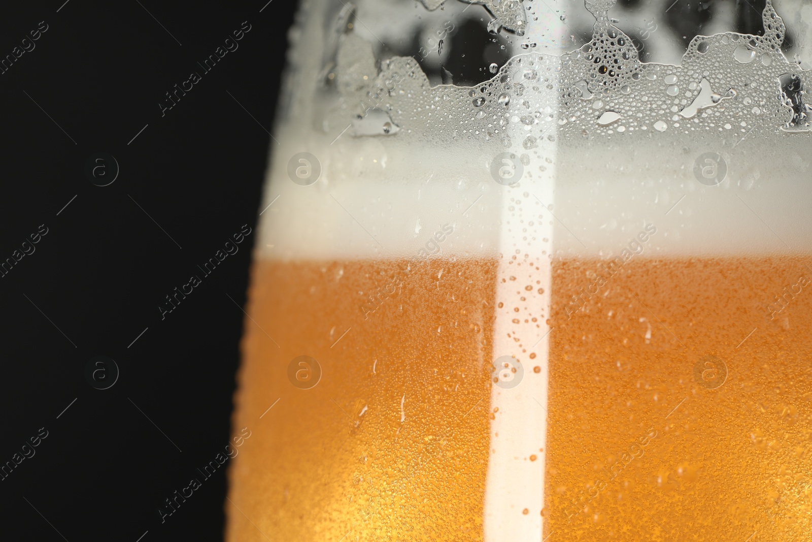 Photo of Glass of beer with condensation drops on black background, macro view