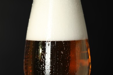 Photo of Glass of beer with condensation drops on black background, macro view