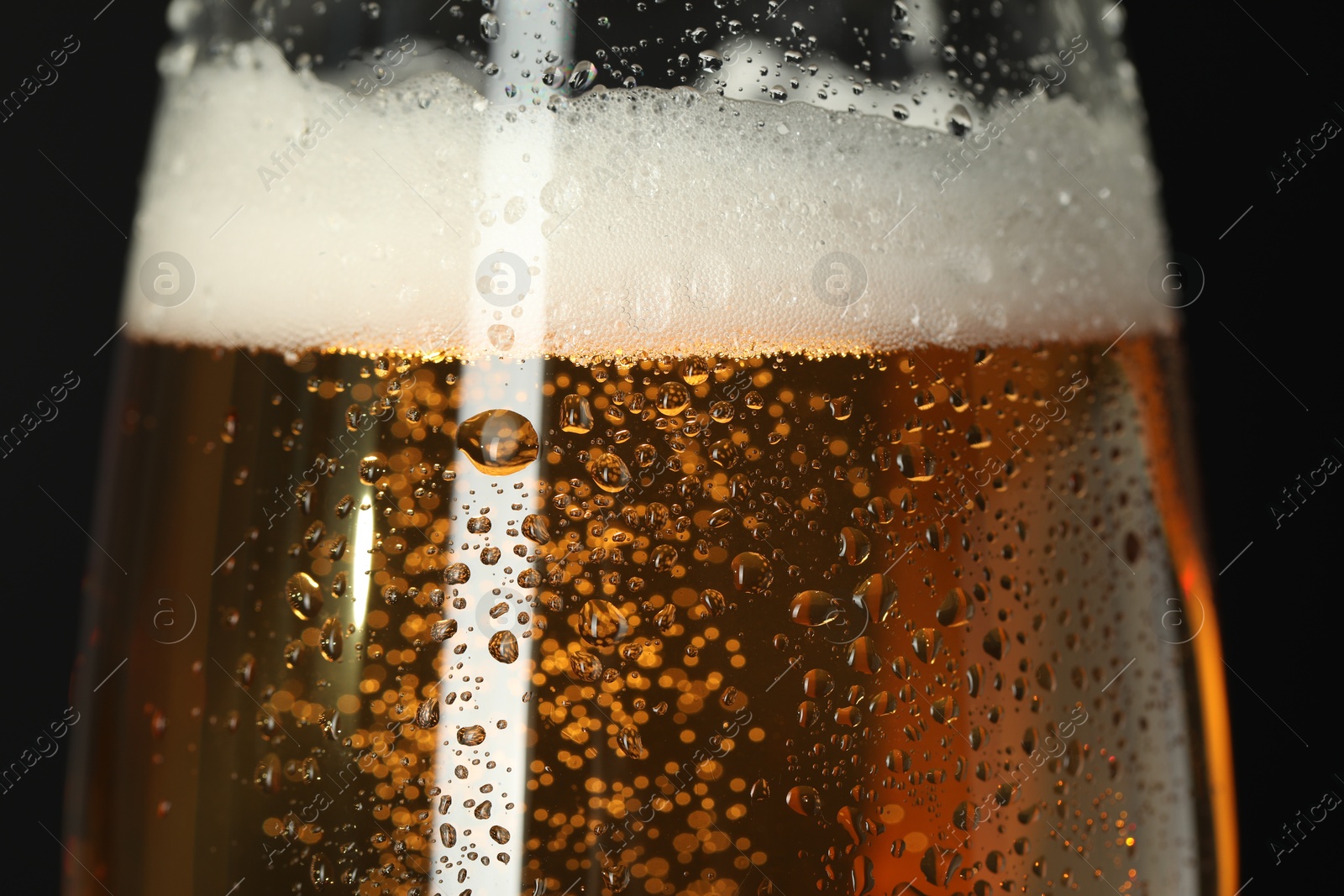 Photo of Glass of beer with condensation drops on black background, macro view