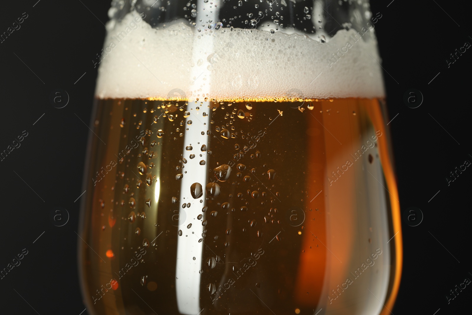 Photo of Glass of beer with condensation drops on black background, closeup