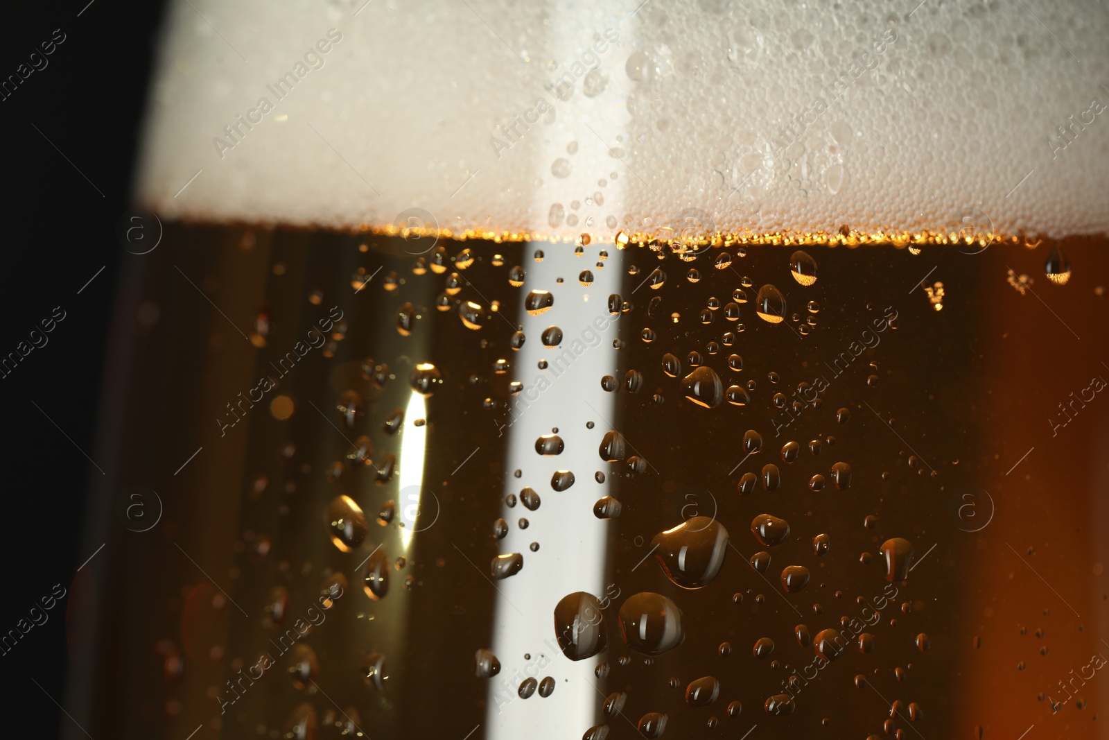 Photo of Glass of beer with condensation drops on black background, macro view