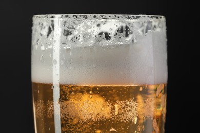 Photo of Glass of beer with condensation drops on black background, closeup