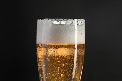 Photo of Glass of beer with condensation drops on black background, closeup