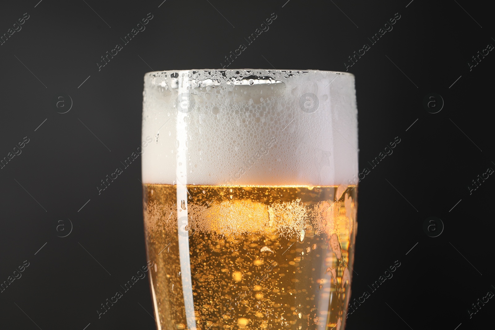 Photo of Glass of beer with condensation drops on black background, closeup