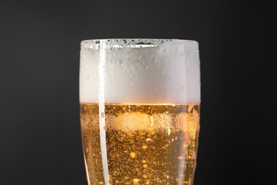 Photo of Glass of beer with condensation drops on black background, closeup