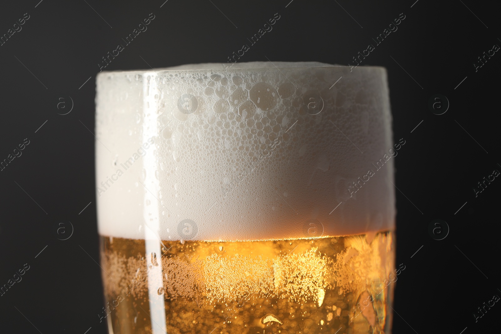 Photo of Glass of beer with condensation drops on black background, closeup