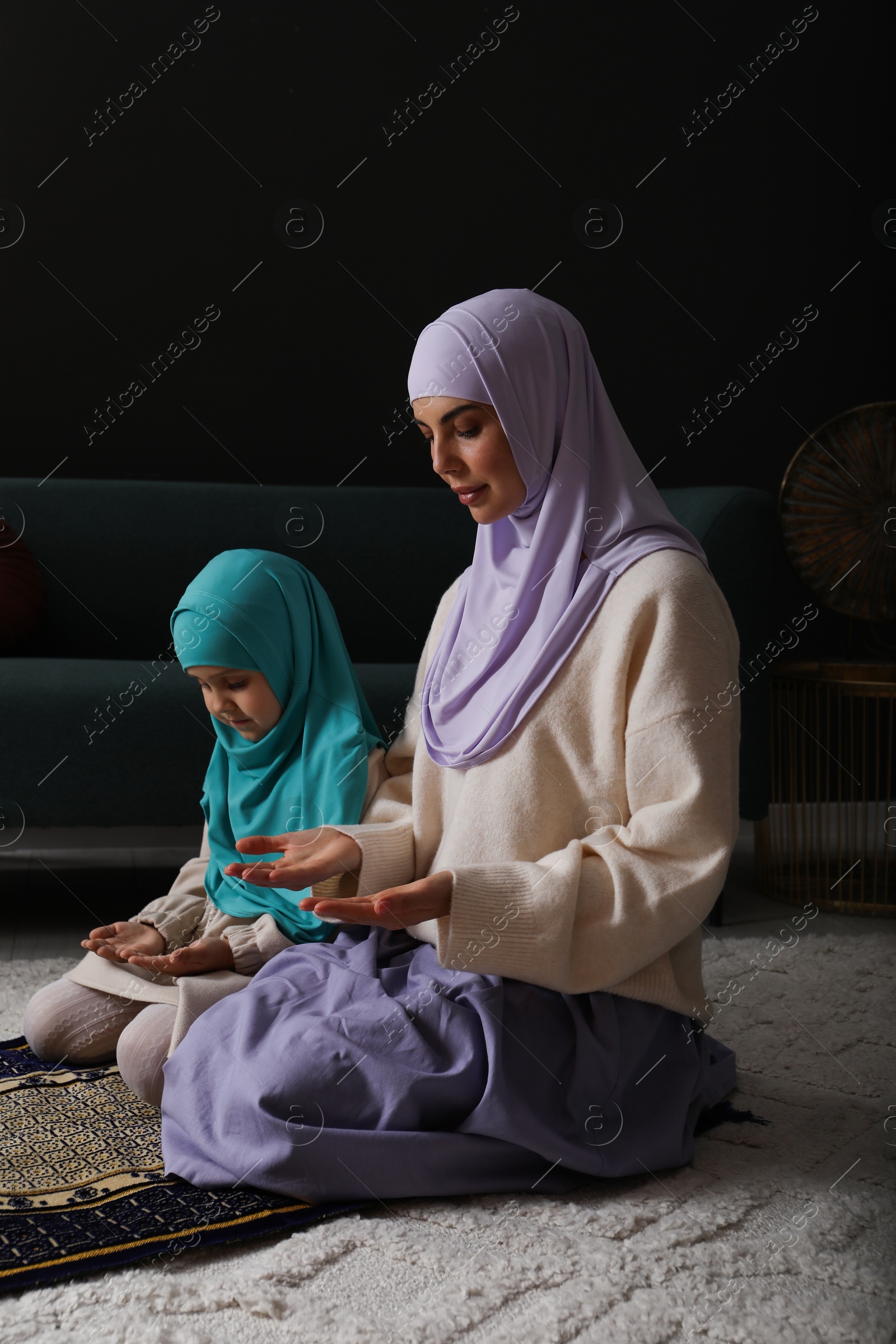 Photo of Muslim woman and her daughter praying on mat at home