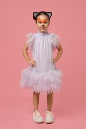 Photo of Cute girl with painted face and ears as cat on pink background