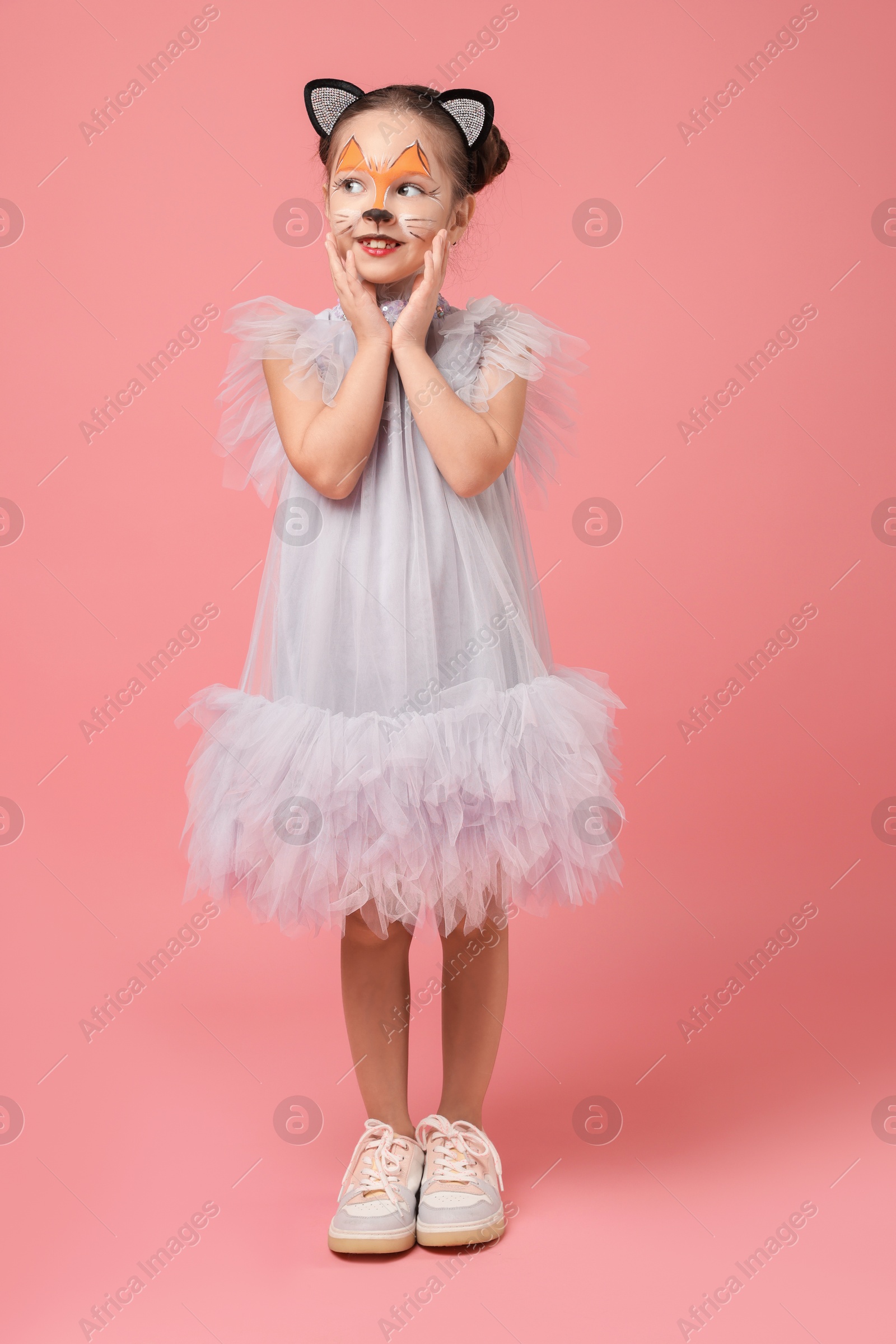 Photo of Cute girl with painted face and ears as cat on pink background