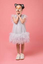 Photo of Cute girl with painted face and ears as cat on pink background