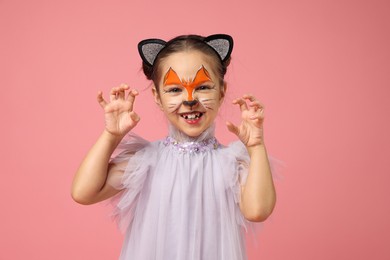 Photo of Cute girl with painted face and ears as cat on pink background