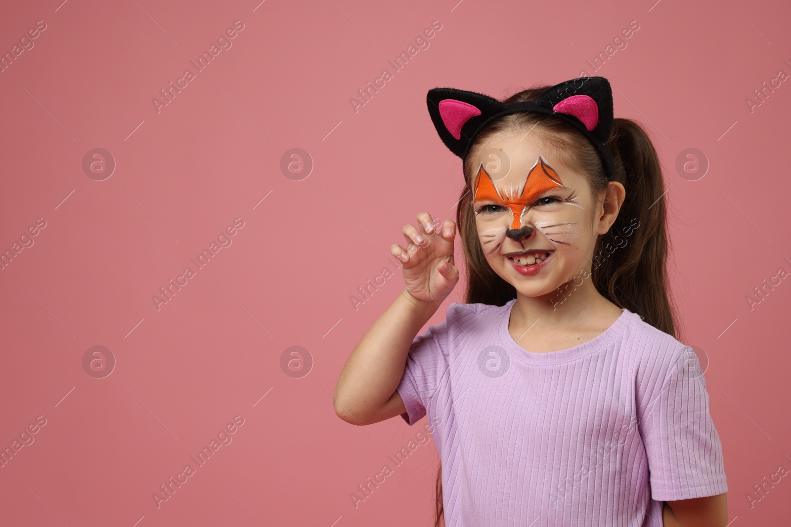 Photo of Cute girl with painted face and ears as cat on pink background, space for text