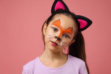 Cute girl with painted face and ears as cat on pink background