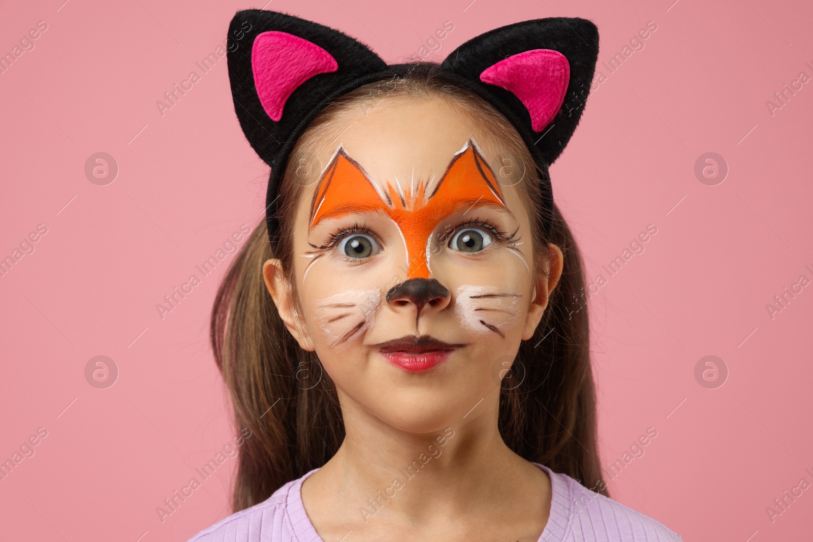 Photo of Cute girl with painted face and ears as cat on pink background