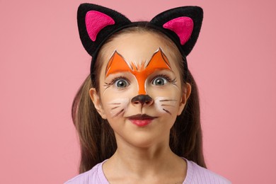 Photo of Cute girl with painted face and ears as cat on pink background