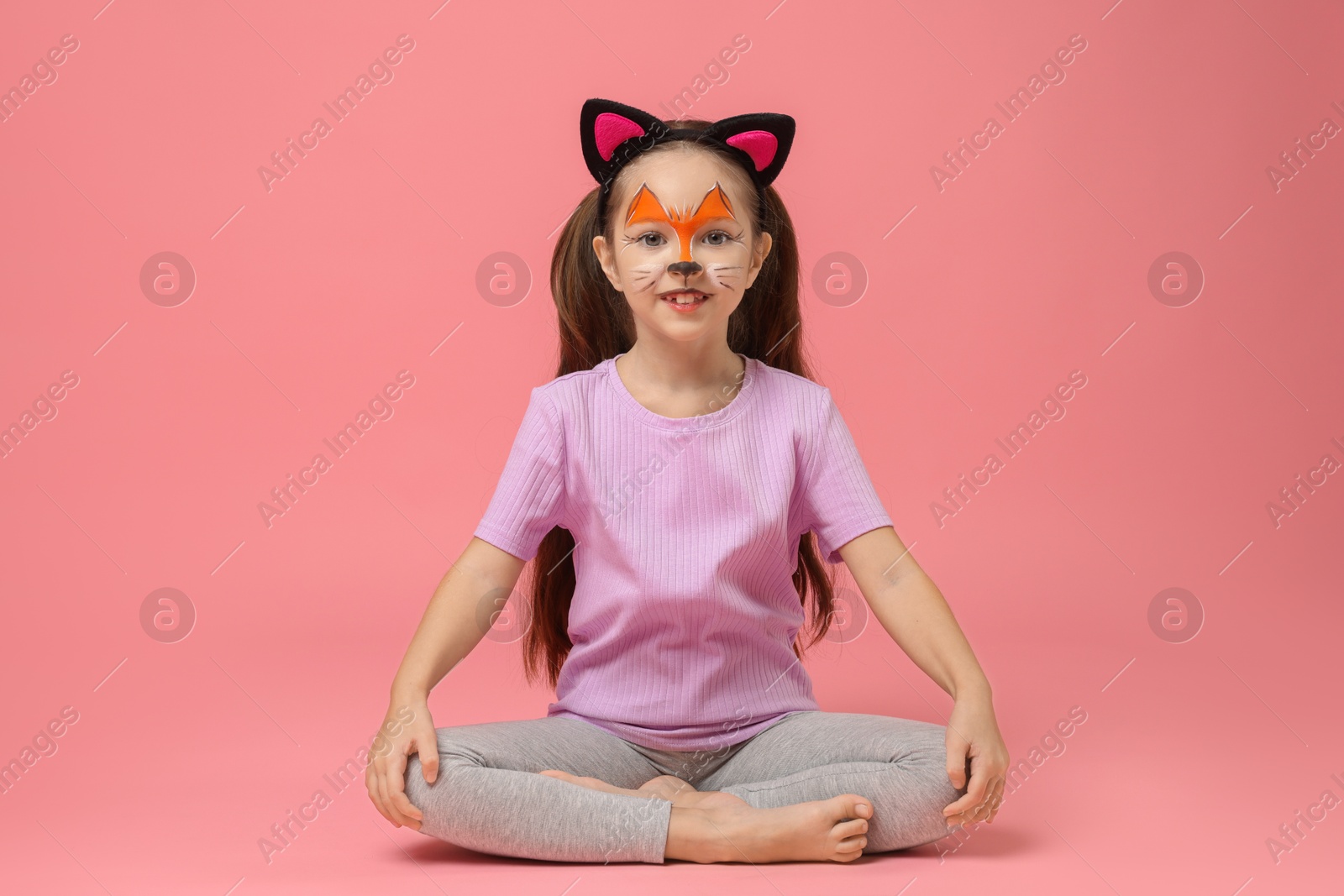 Photo of Cute girl with painted face and ears as cat on pink background