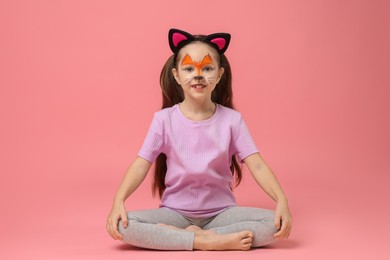 Photo of Cute girl with painted face and ears as cat on pink background