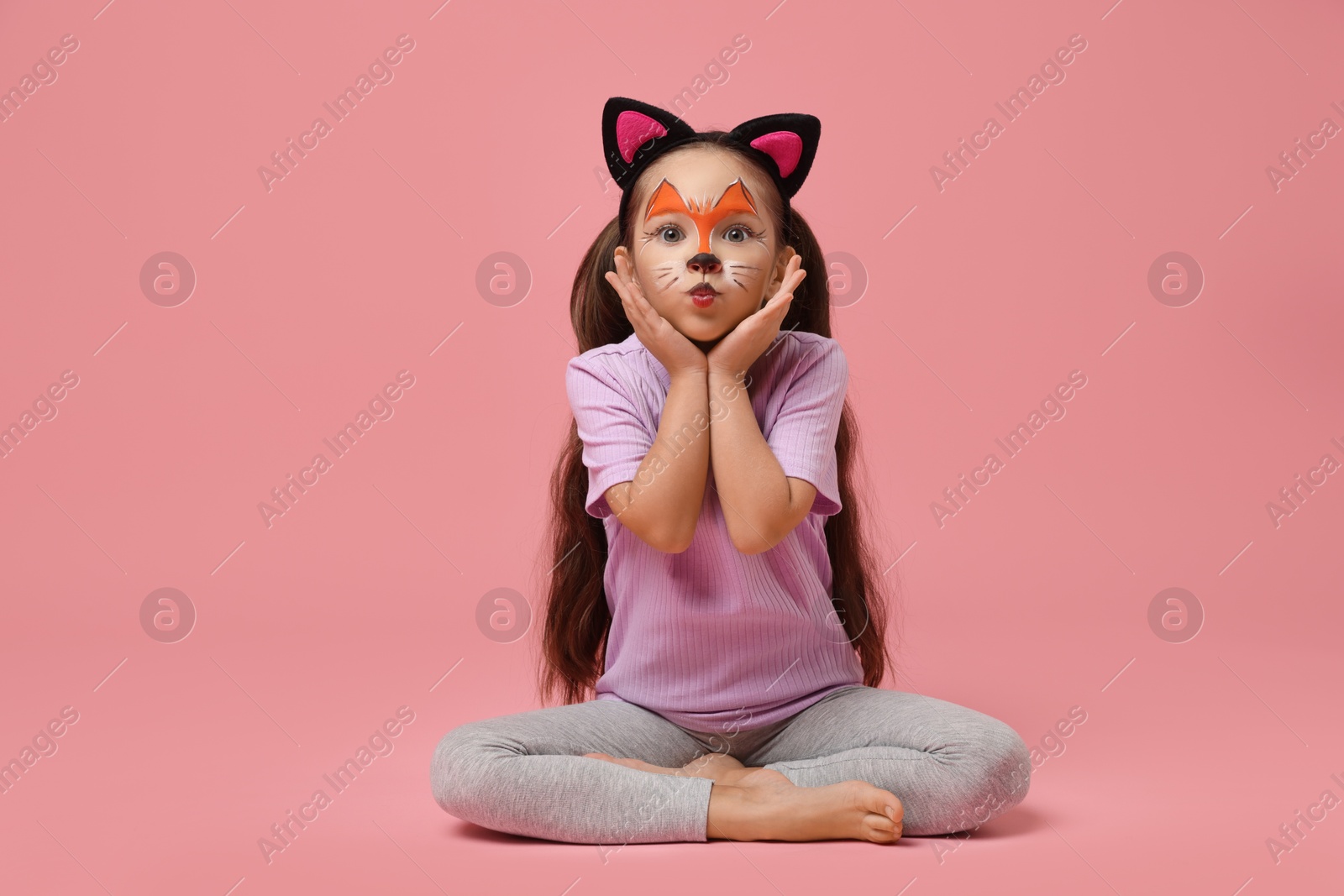 Photo of Cute girl with painted face and ears as cat on pink background