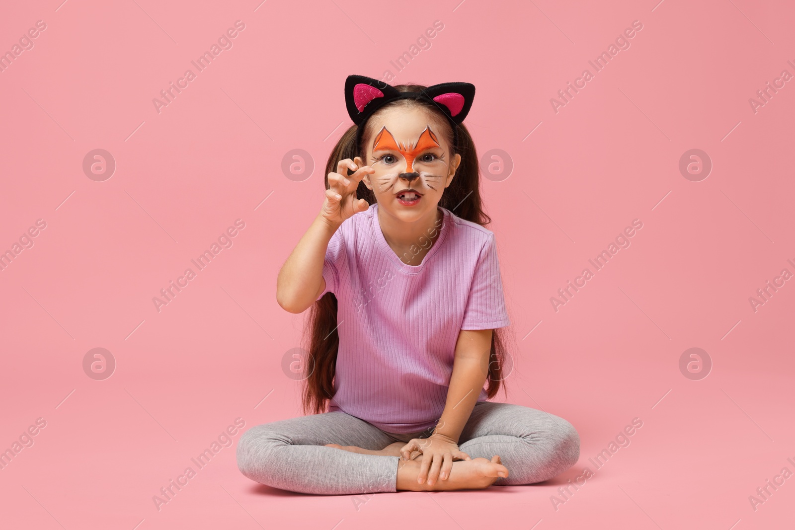 Photo of Cute girl with painted face and ears as cat on pink background