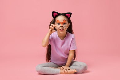 Cute girl with painted face and ears as cat on pink background