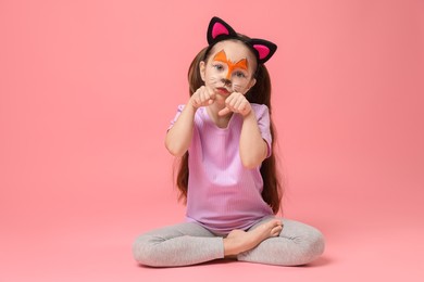 Photo of Cute girl with painted face and ears as cat on pink background