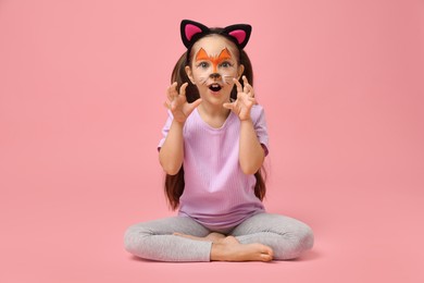 Cute girl with painted face and ears as cat on pink background